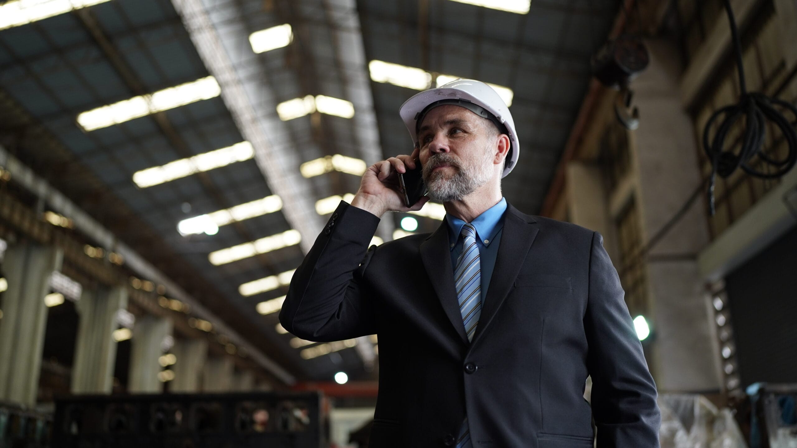 Businessman in factory warehouse talking on mobile, representing Ruby Receptionist's contractor answering service.